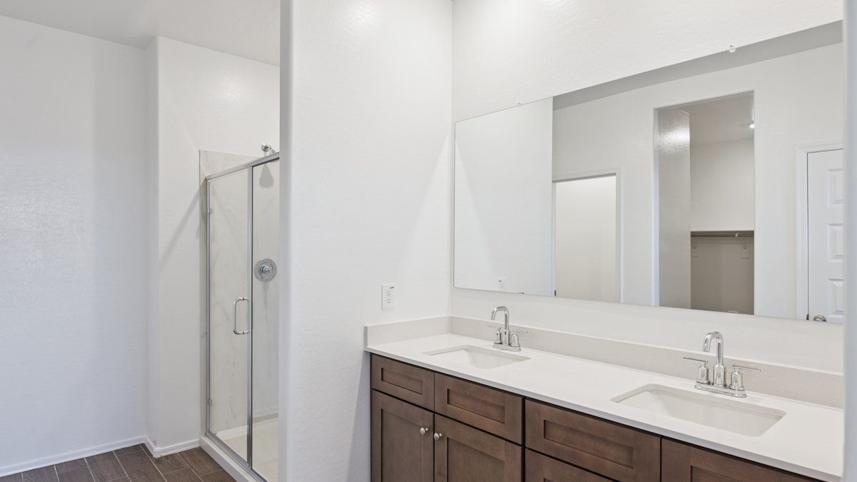 Modern primary bathroom with double vanities, quartz countertops with a walk-in shower and a walk-in closet.
