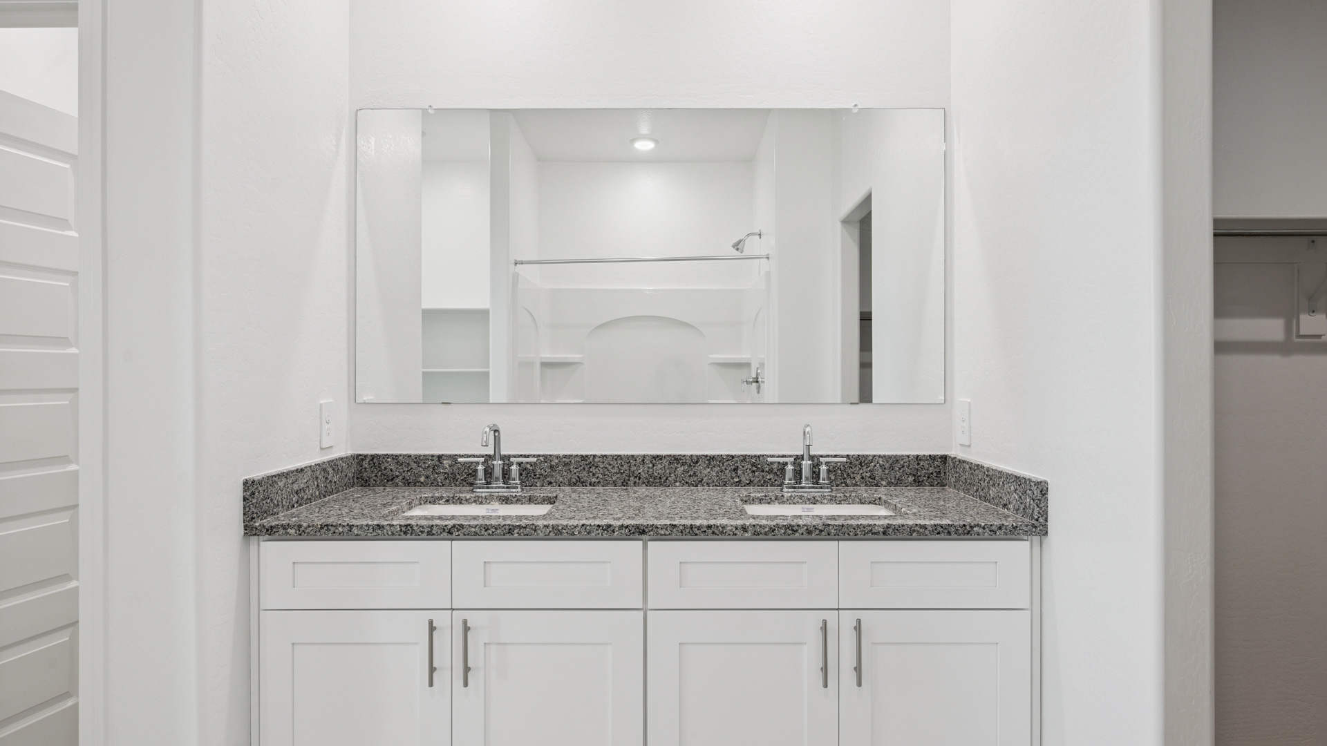 Modern primary bathroom with double vanity, granite countertops with a walk-in shower and a walk-in closet.