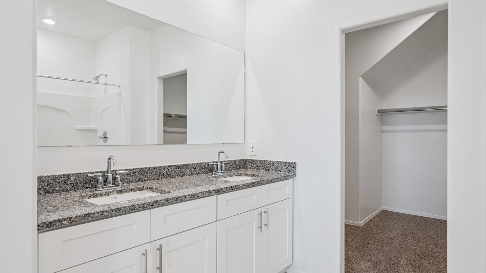 Modern primary bathroom with double vanity, granite countertops with a walk-in shower and a walk-in closet.