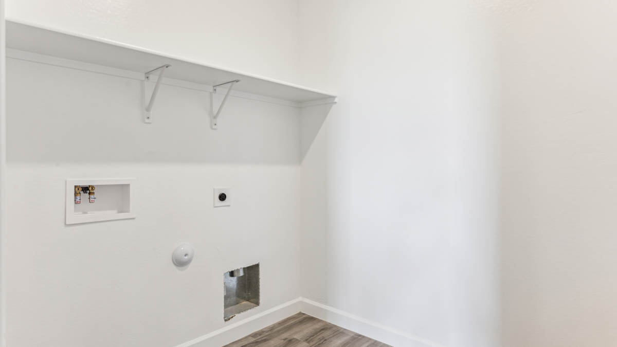 Spacious laundry room with washer and dryer connections and shelving for storage.