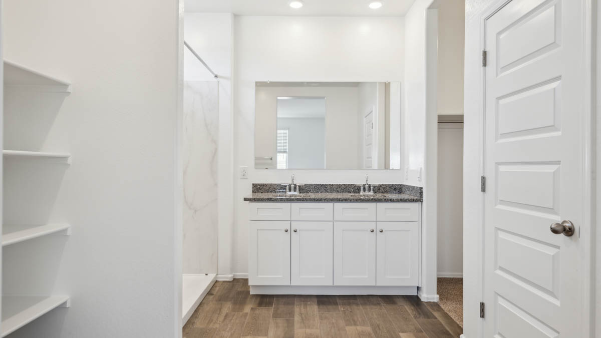 Modern primary bathroom with double vanity, granite countertops with a walk-in shower and a walk-in closet.