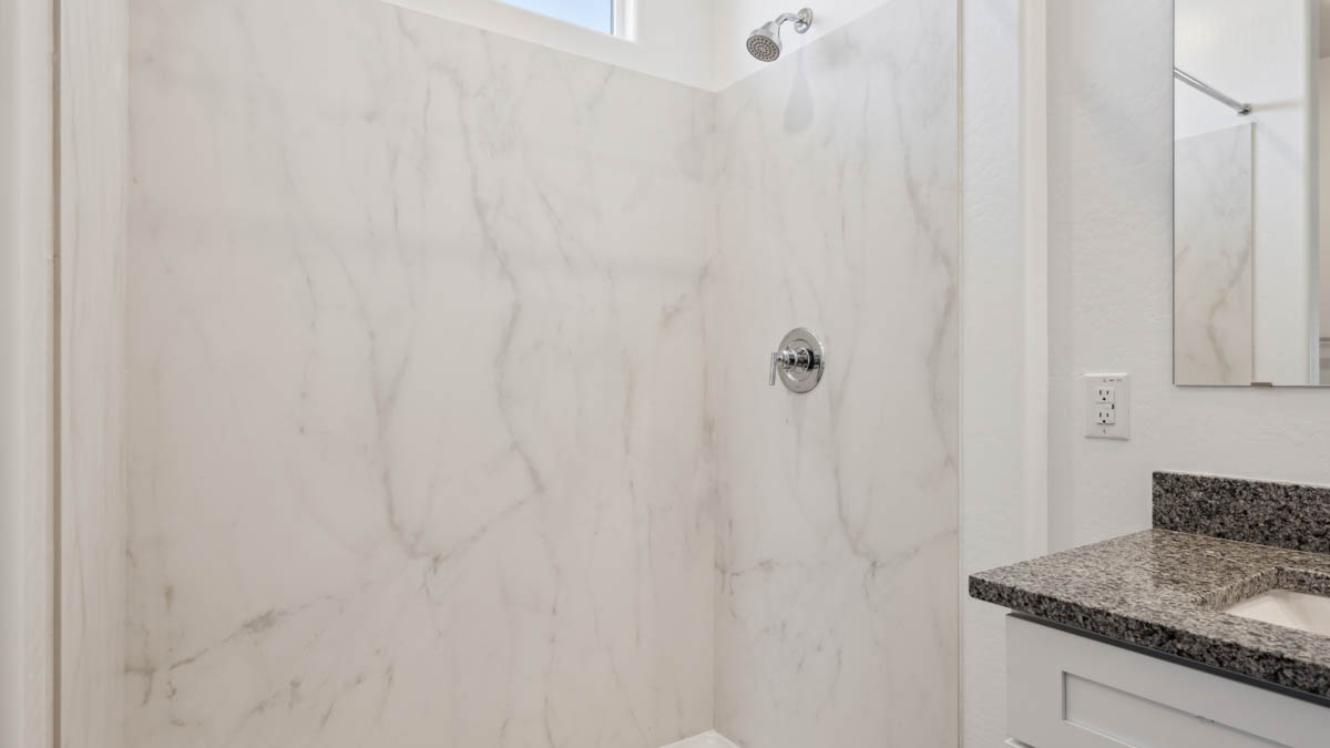 Modern primary bathroom with double vanity, granite countertops with a walk-in shower and a walk-in closet.