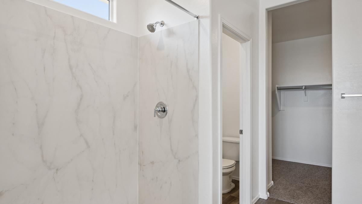 Modern primary bathroom with double vanity, granite countertops with a walk-in shower and a walk-in closet.