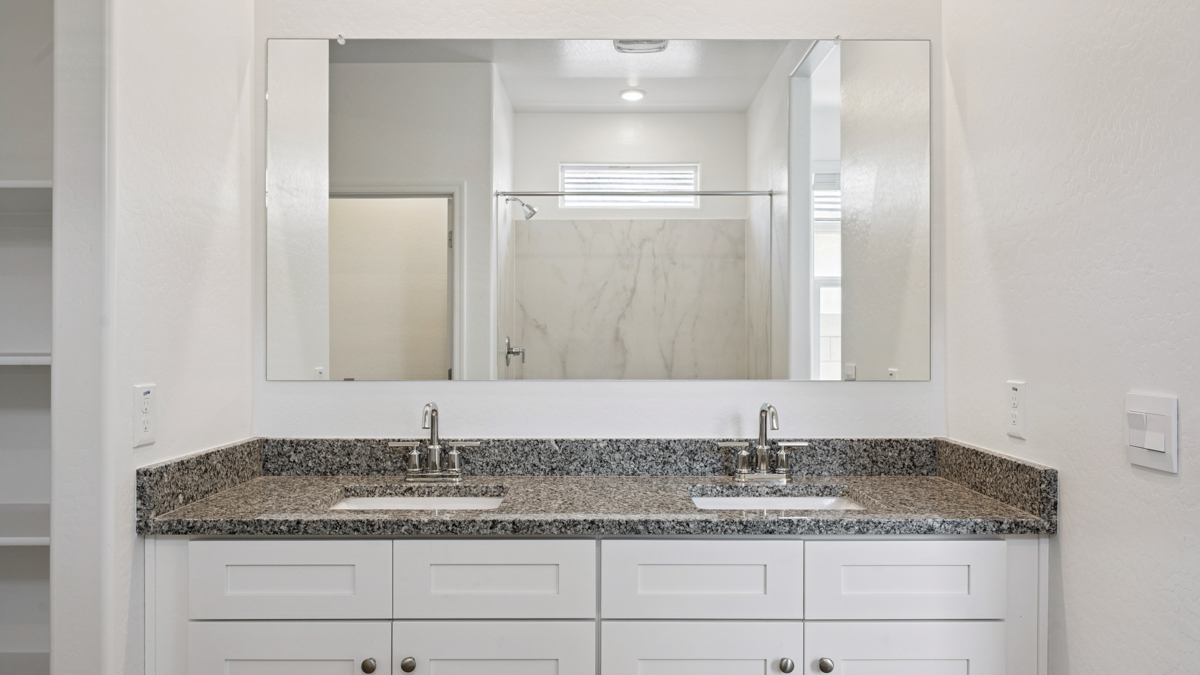 Modern primary bathroom with double vanity, granite countertops with a walk-in shower and a walk-in closet.