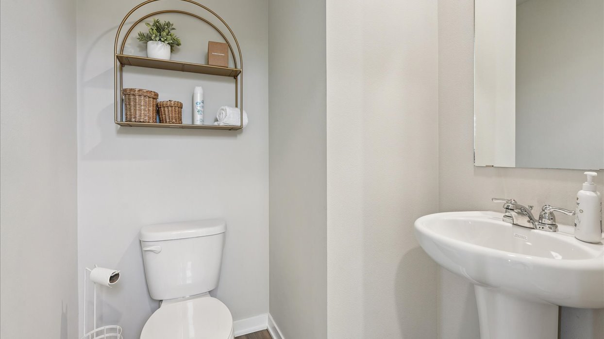 Half bath with hallway door open, pedestal sink, mirror, and stylish polished faucet on main level