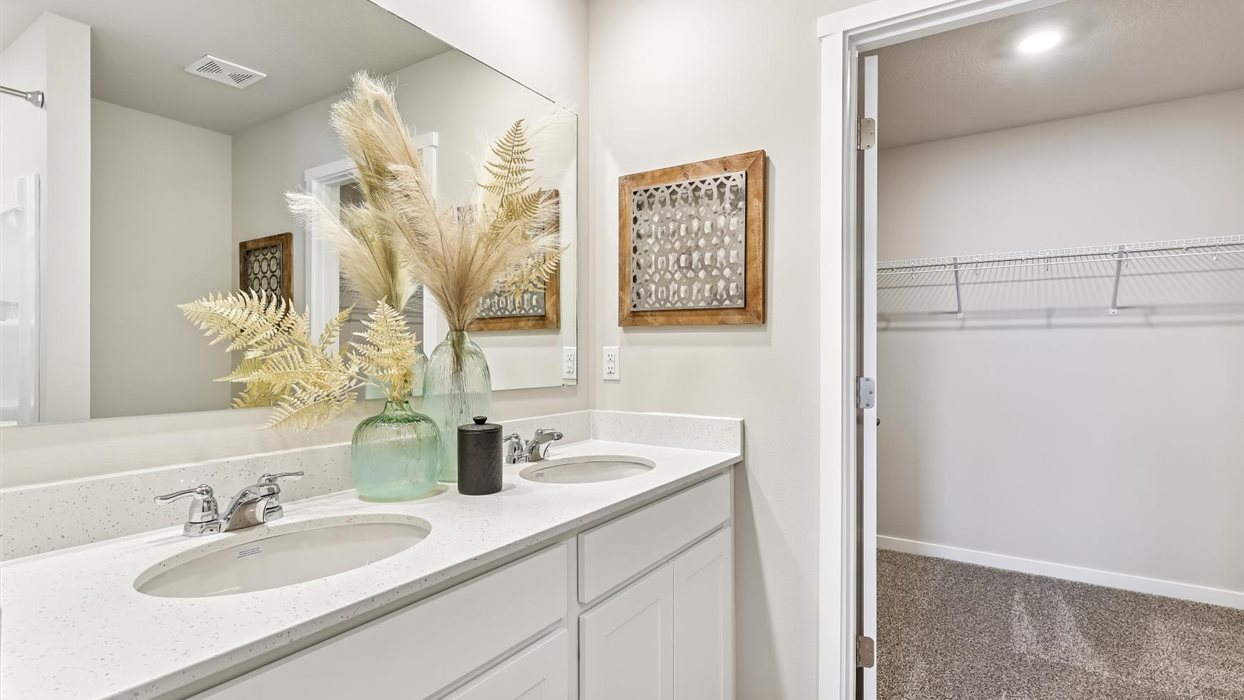 primary bedroom with large mirror and dual sinks with view of walk-in closet