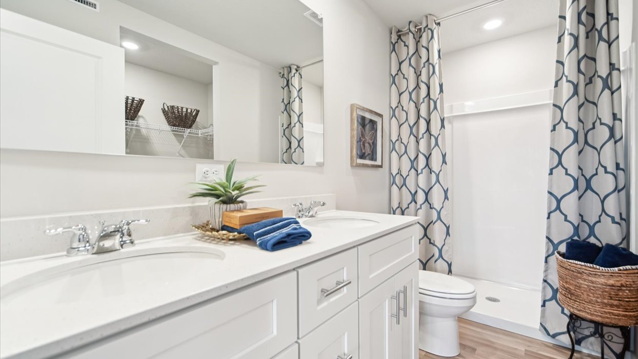 primary bathroom with large mirror and dual sinks with white cabinets