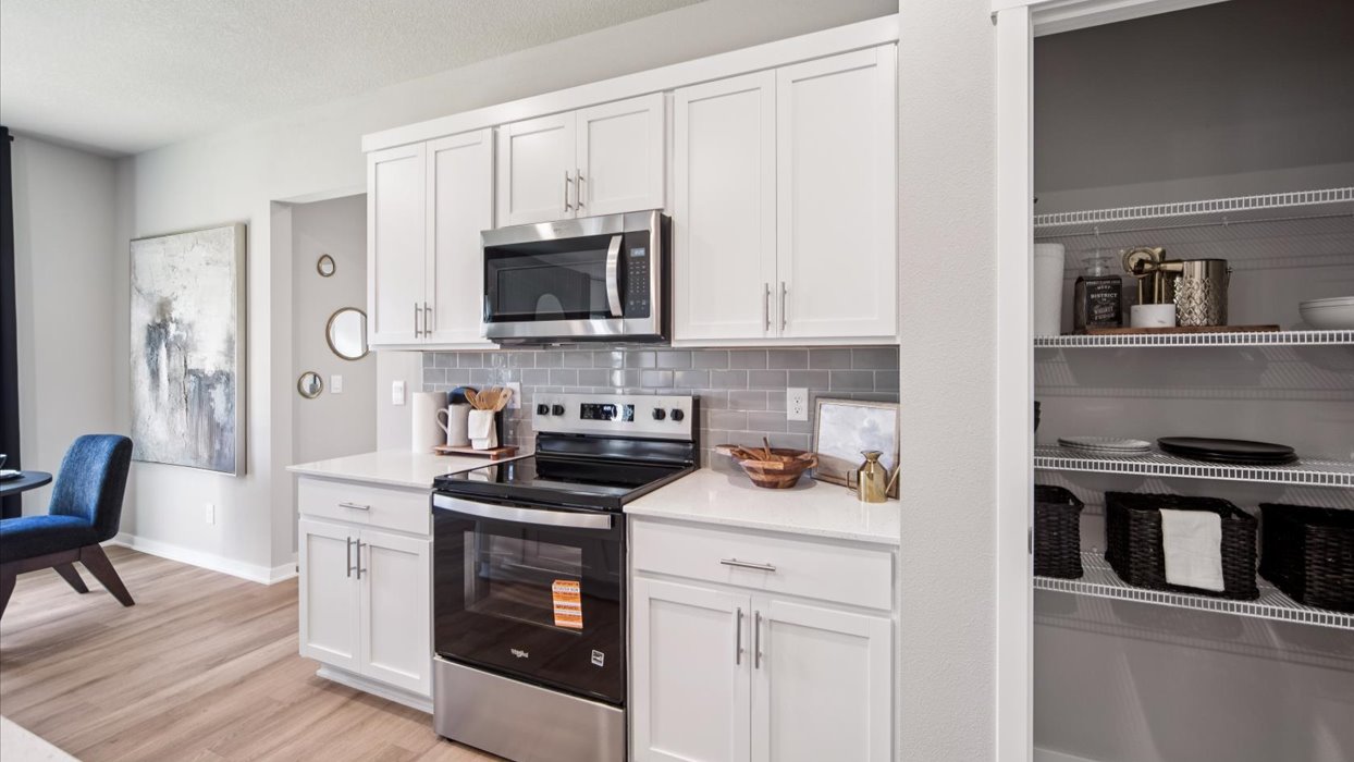 Kitchen island with sink, pantry, cabinetry, and view toward the front door supporting daily prep and organization. Edgewood Trail