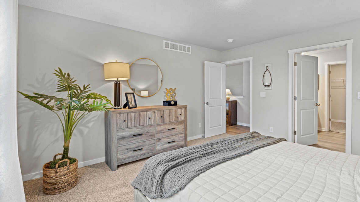 Primary bedroom with large fake plant and lamp on dresser
