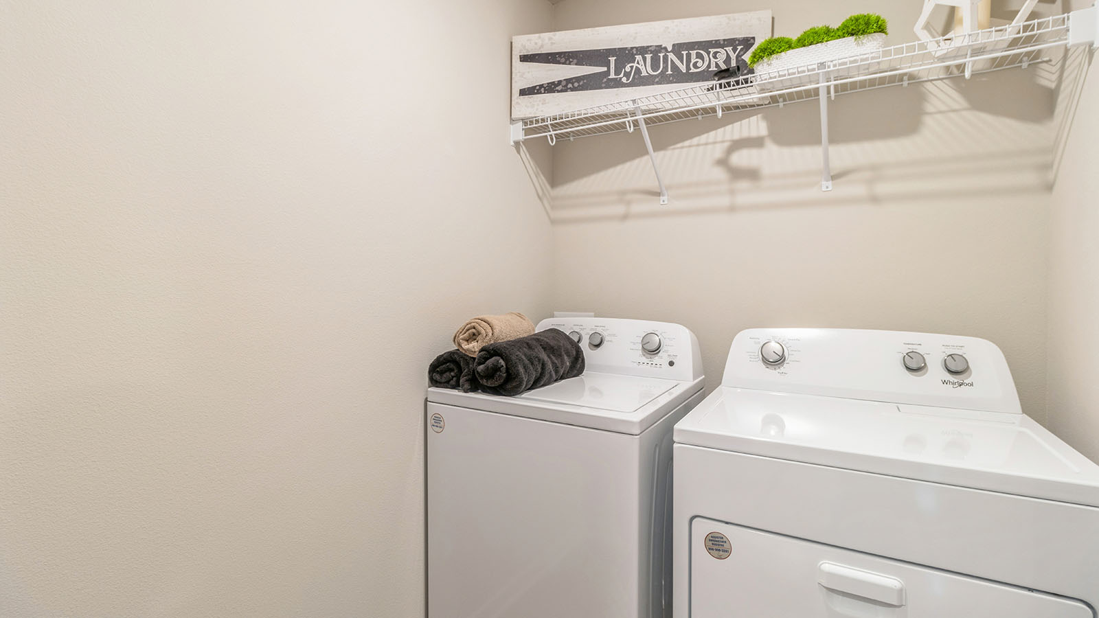 Modern laundry room with new washer dryer in Summercrest by D.R. Horton with upper shelving and clean design finishes