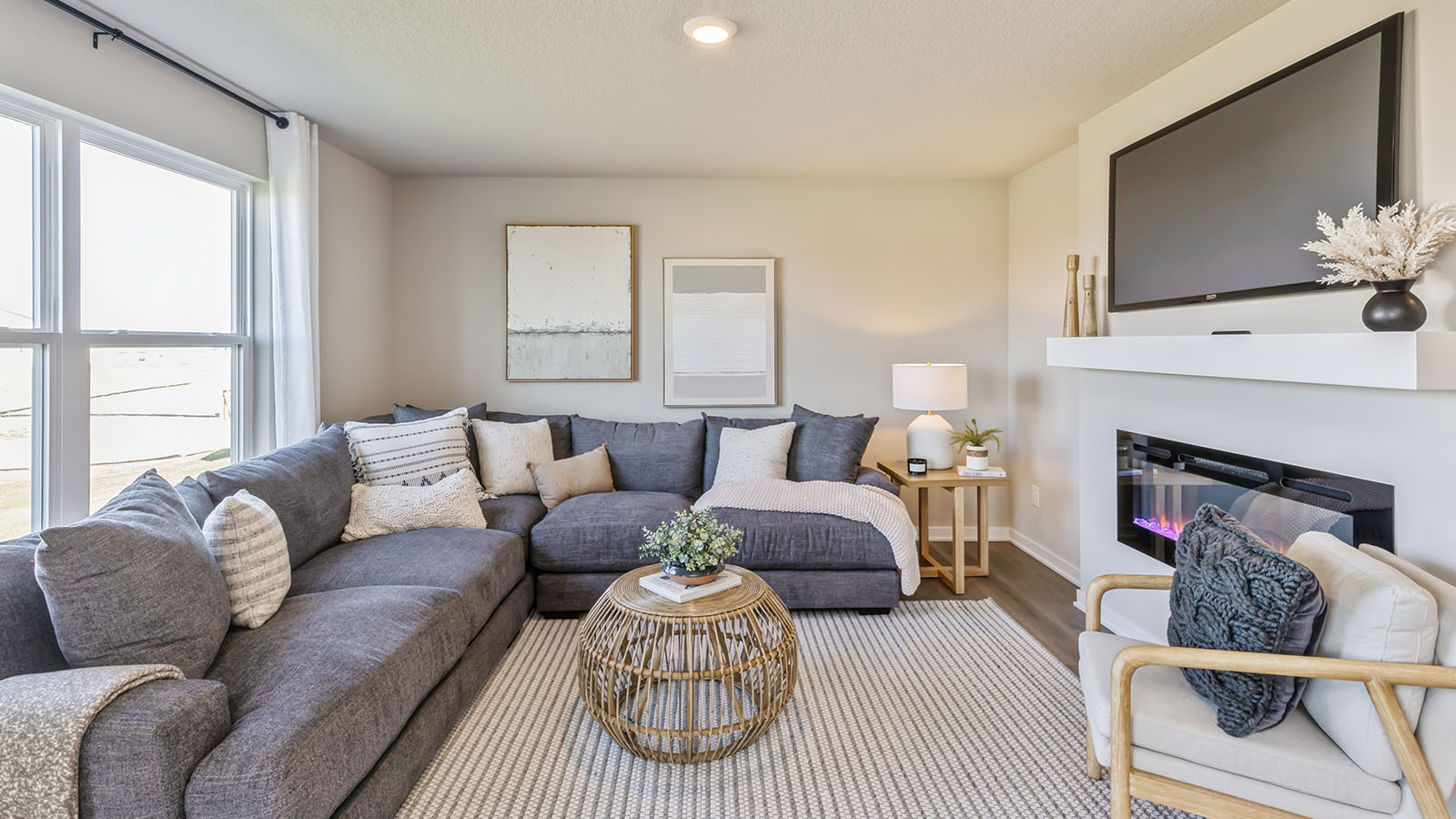 Living area with a large grey sectional, a white chair, fireplace, and a large window.