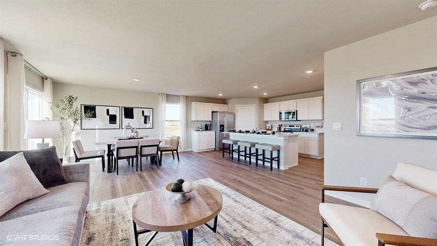 A spacious, modern open-plan living area with a kitchen and dining setup. Neutral tones, cozy seating, and large windows create a bright, inviting ambiance.