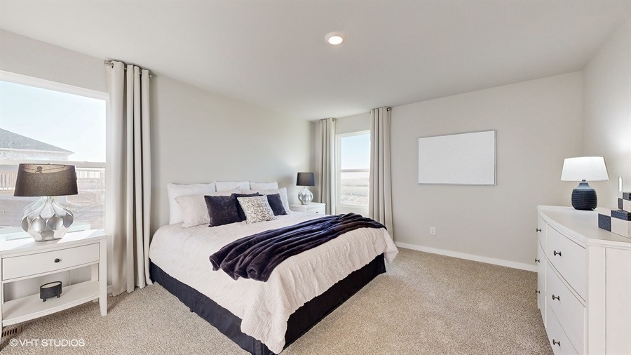 A bright bedroom with neutral tones features a large bed with white and purple bedding, flanked by white nightstands and windows. The atmosphere is calm and inviting.