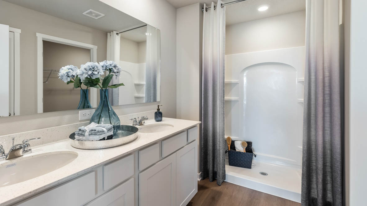 Ensuite bath room has a double vanity sink with quartz countertops, white shaker-style cabinets and a white walk-in shower.