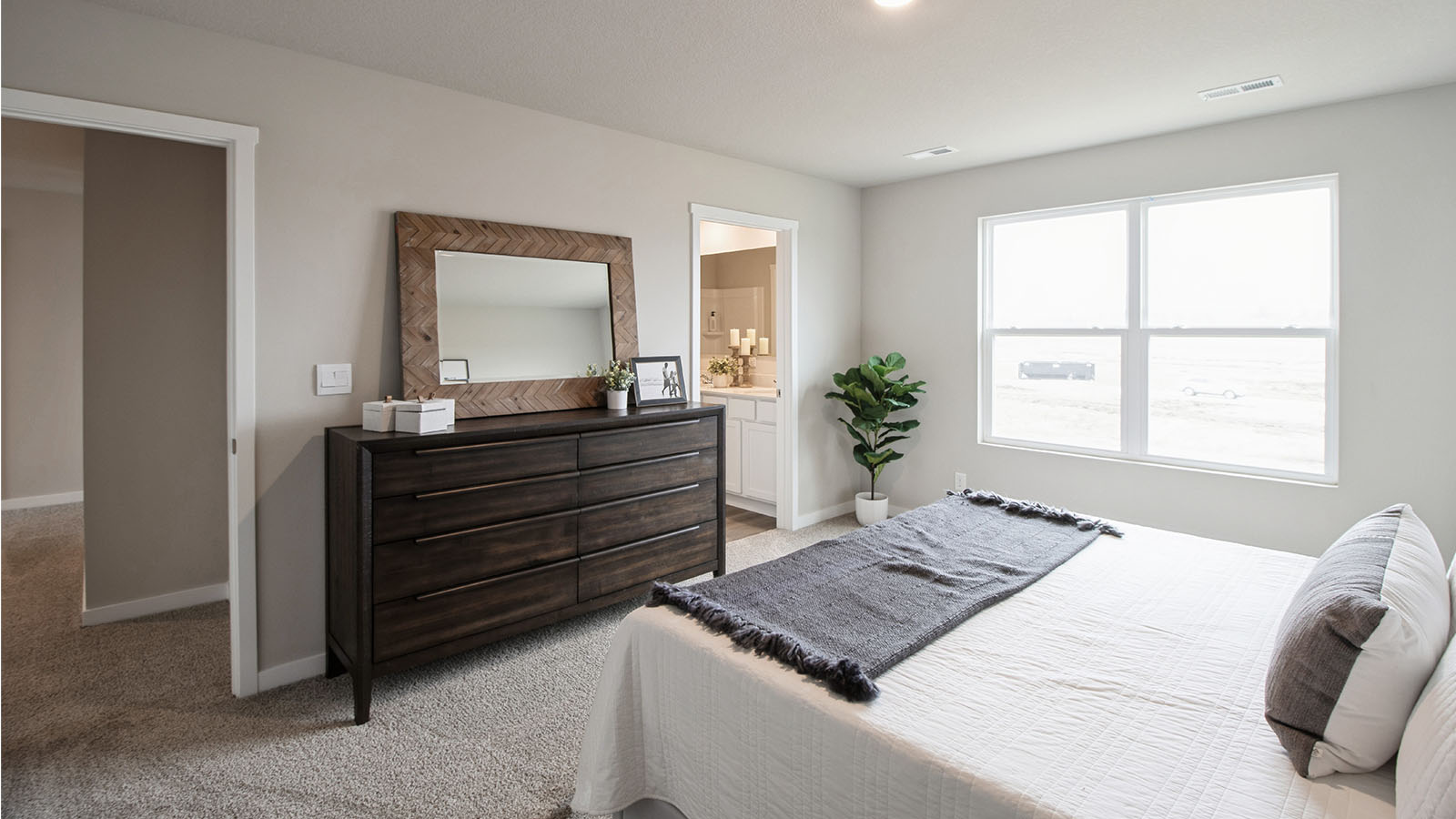 Primary bedroom with large window and white bed with dark wood dresser