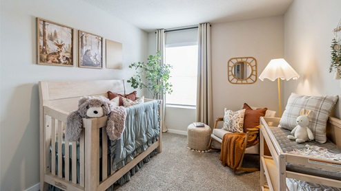 First bedroom staged as a nursery with small window and crib and nursing table