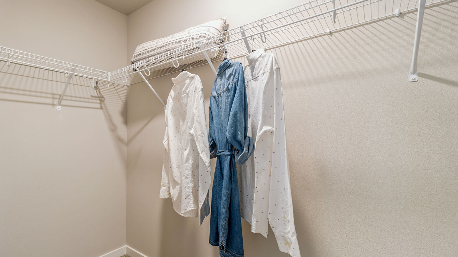 Large walk-in closet with white shelving and hanging rods with clothes hanging from them