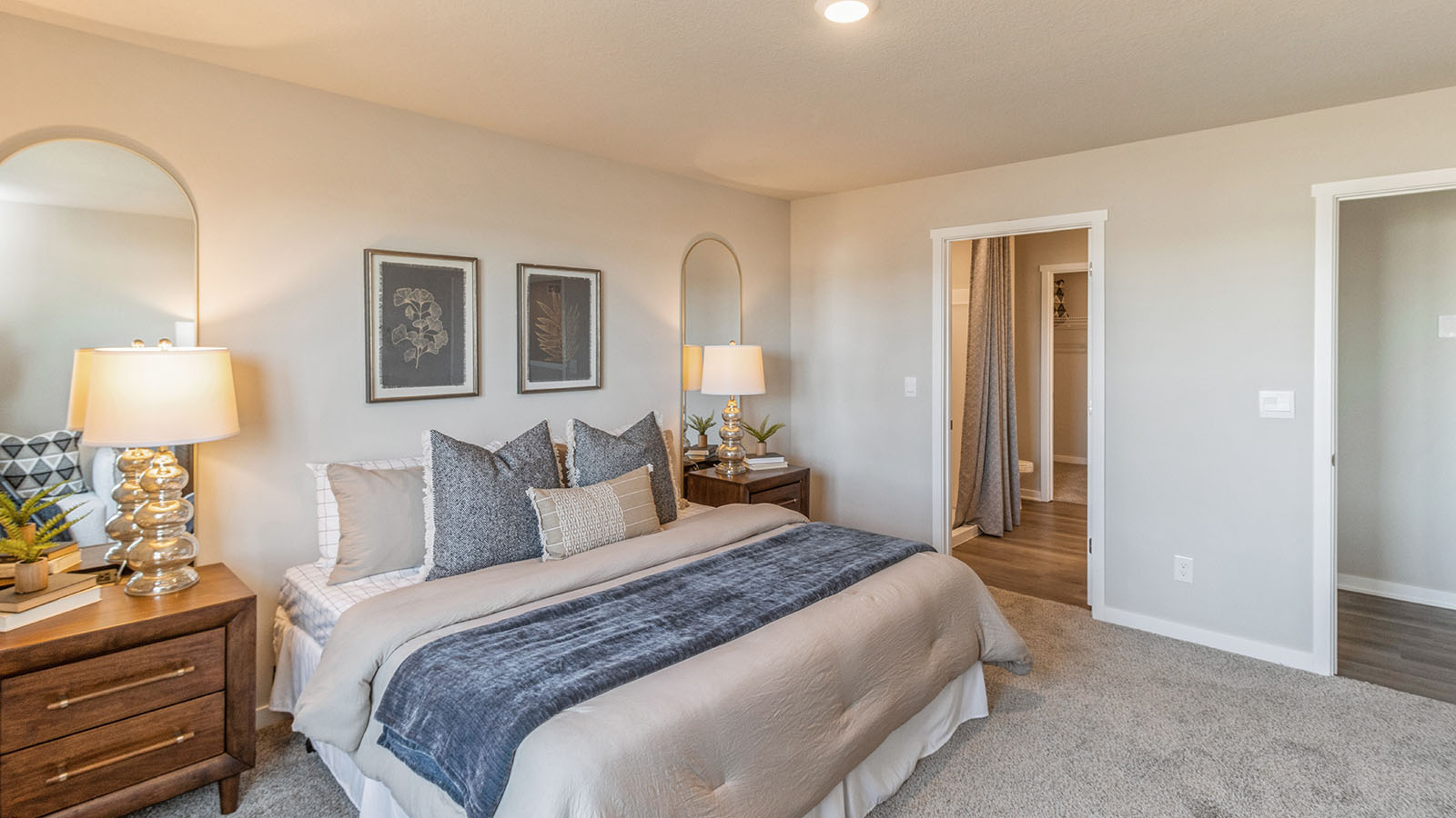 Bright primary bedroom with large tan bed and view of primary bathroom
