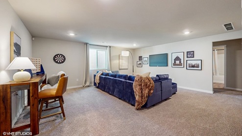A recreation room with a high-top table and chairs and a lush sectional facing a wall-mounted TV and artwork.