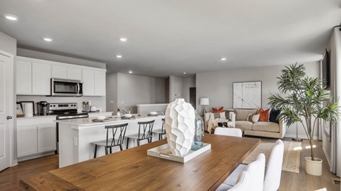 Wooden dining table with seating for six and a view of the kitchen and living room beyond.