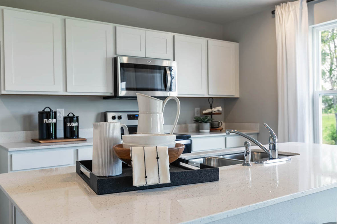 Close-up view of decor on a kitchen island showing white, shaker-style upper and lower cabinetry in the background with a built-in, stainless-steel microwave and range below.