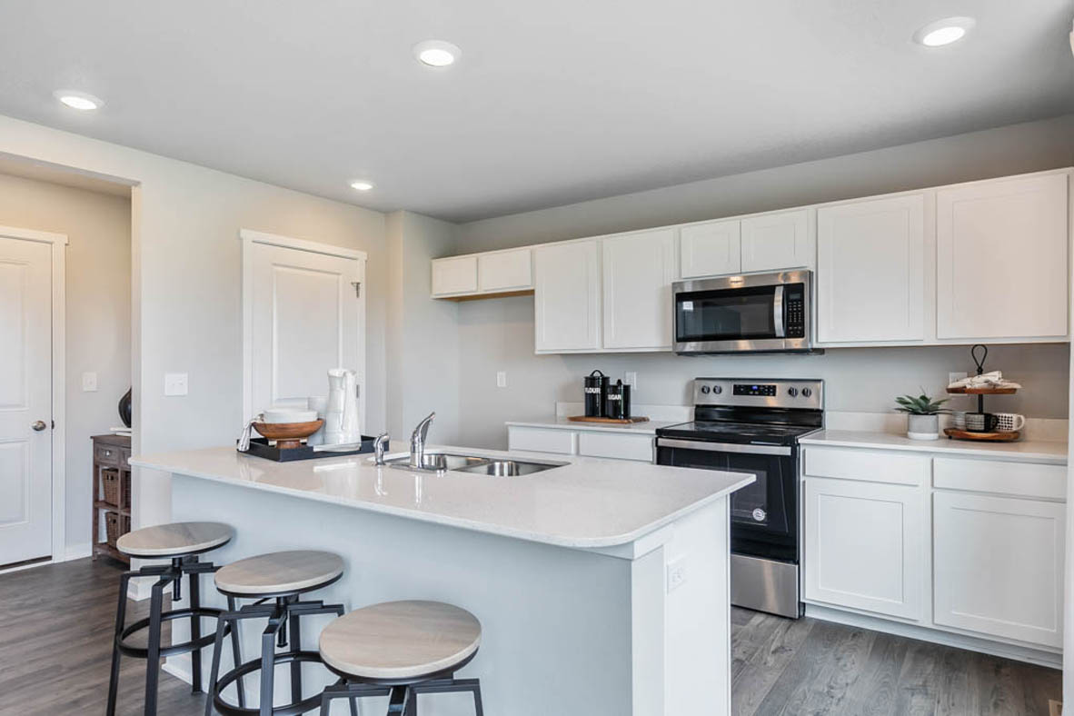 Kitchen with white cabinets, stainless-steel appliances, and an island with an extended countertop and space for three barstools.