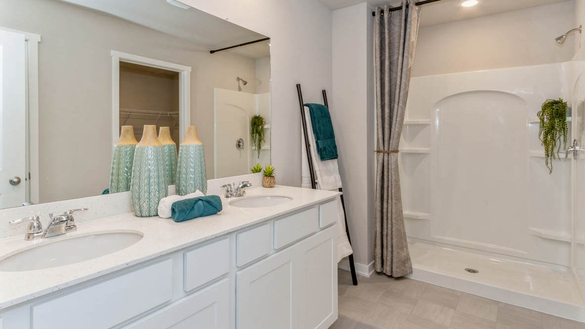 Primary bathroom in the Neuville with a double vanity with white, shaker-style cabinets and a walk-in shower stall.