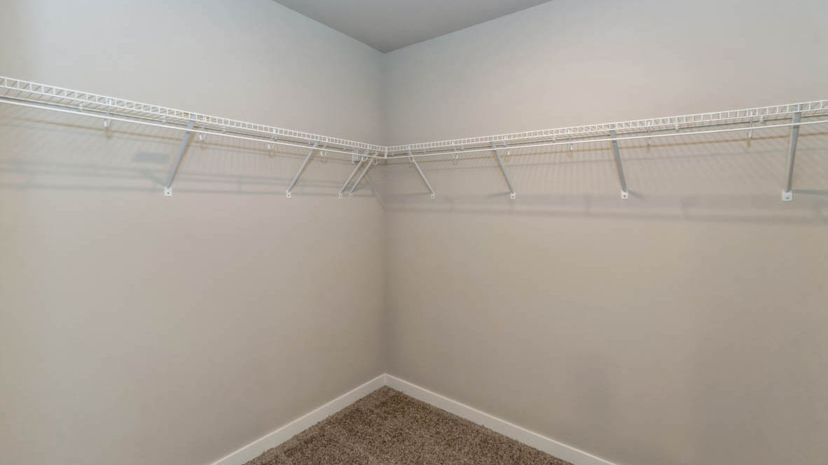 Large, walk-in closet off of the primary bathroom in the Neuville with wire shelving and hanging rods across two walls.
