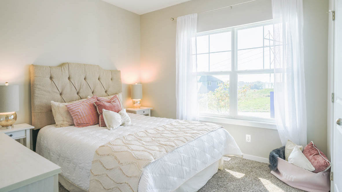 One of the Neuville plan's secondary bedrooms with a double bed, two nightstands, and a dresser with a large window allowing lots of natural light.