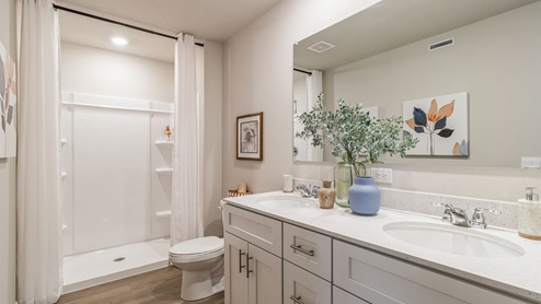primary bedroom with large mirror and dual sinks and white cabinetry