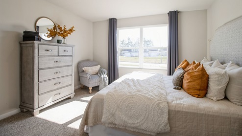 Primary bedroom with large dresser and tan bed