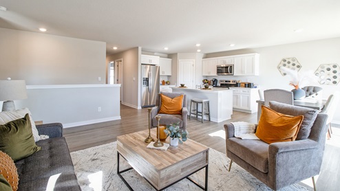 Cozy living room with grey chairs and wood coffee table overlooking the modern kitchen