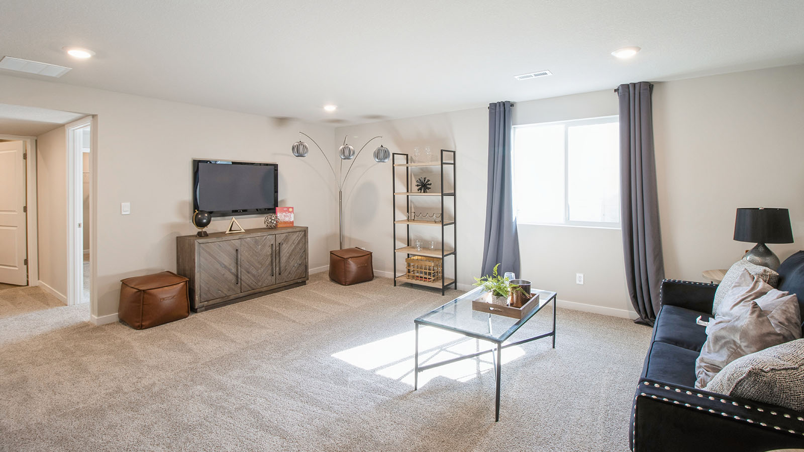 Spacious finished basement with gray carpet, wooden TV stand, mounted TV, and a window