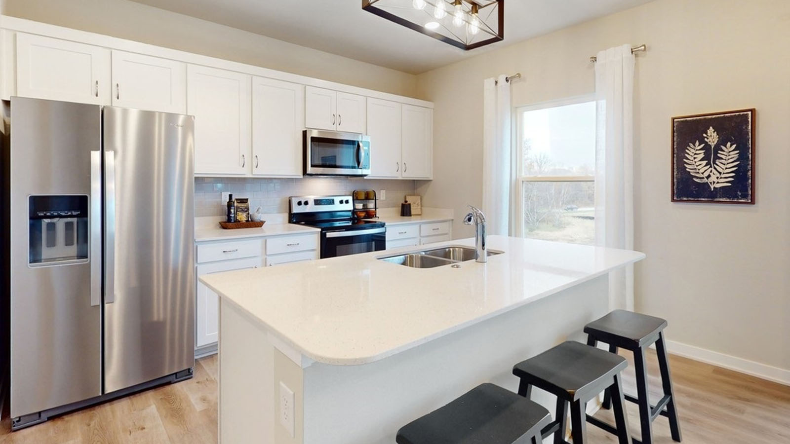 Kitchen has an island sink with quartz countertops, white shaker-style cabinets, white subway style backsplash, stainless steel appliances and a single window.