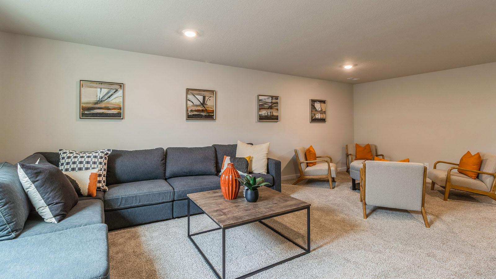 Finished basement with large grey sectional and tan chairs