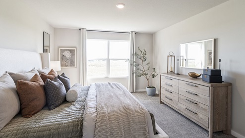 Primary bedroom with large window and bed with wood dresser