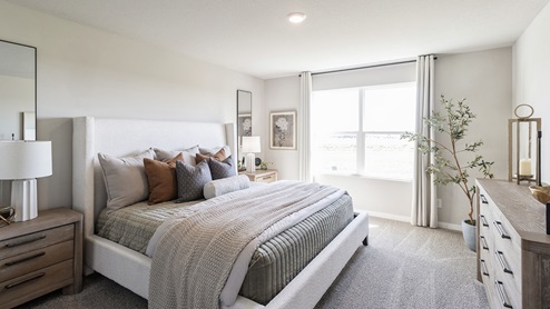 Spacious primary bedroom with grey bed and large window with dresser