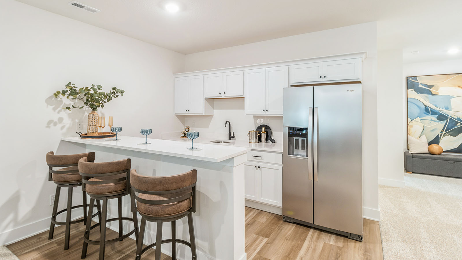 Wet bar in finished basement with white cabinets and island with quartz countertops
