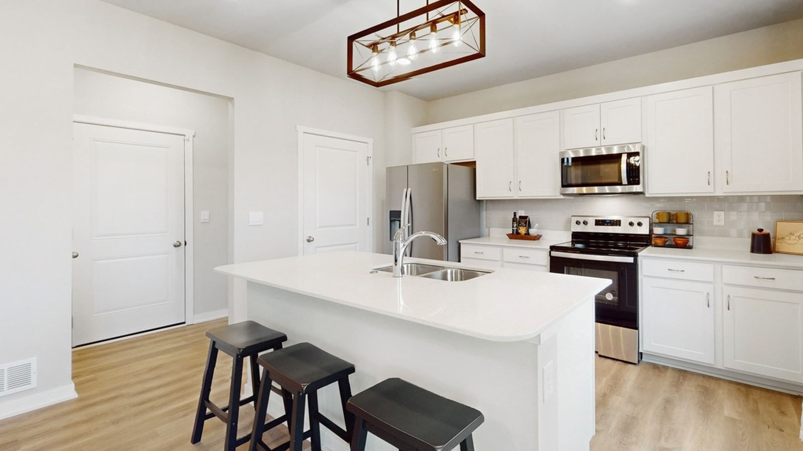 The Bellhaven's kitchen with white, shaker-style cabinetry, quartz countertops, and stainless-steel appliances that features place settings and barstools at the island's countertop seating.