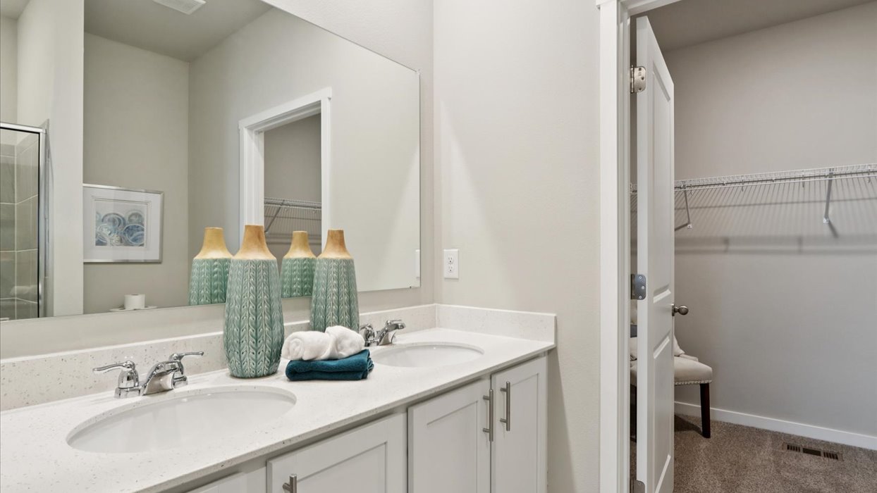 primary bathroom with large mirror and dual sinks with walk-in closet