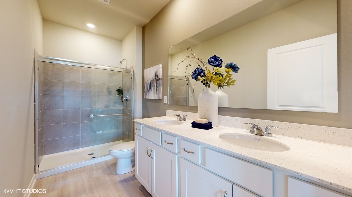 primary bathroom with a walk in shower with glass doors and dual sinks