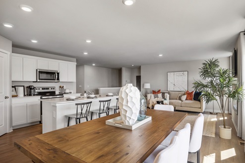 Wooden dining table with seating for six and a view of the kitchen and living room beyond.