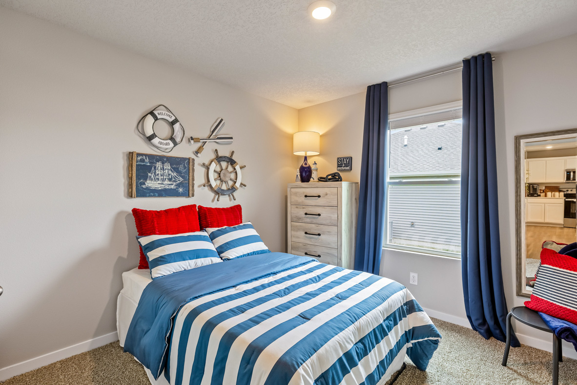 Secondary bedroom in the Roland decorated in a red-and-blue sailing them, with a double bed, chest of drawers, and an accent chair in the corner.