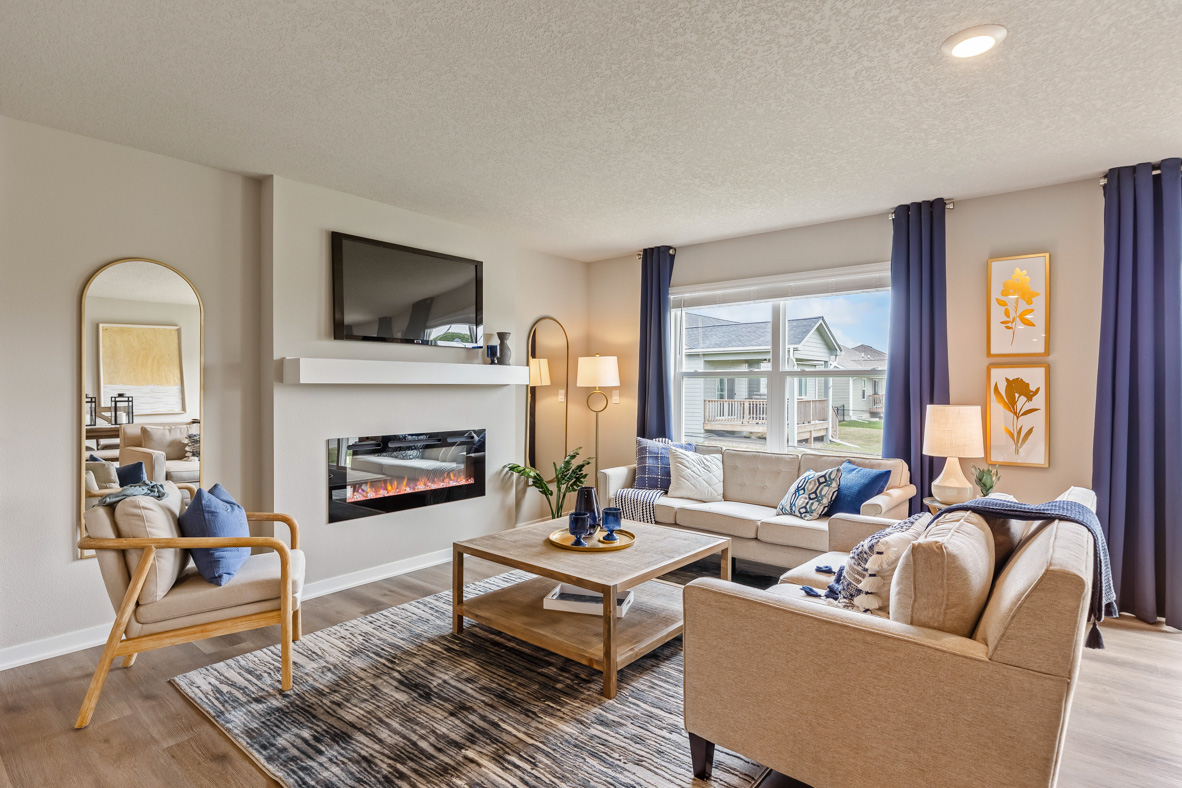 The Roland's living room, with two couches and an accent chair arranged around around a coffee table to face the built-in, electric fireplace, mantel, and wall-mounted TV.