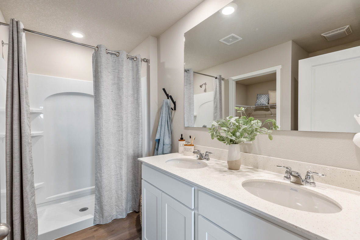 Primary bathroom in the Roland with a double vanity that boasts shaker-style cabinetry and a walk-in shower stall.