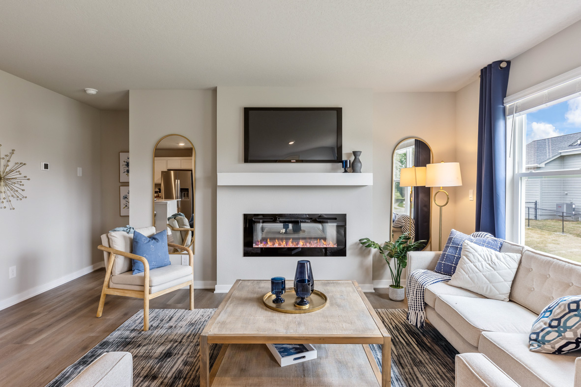 The Roland's living room, with two couches and an accent chair arranged around around a coffee table to face the built-in, electric fireplace, mantel, and wall-mounted TV.