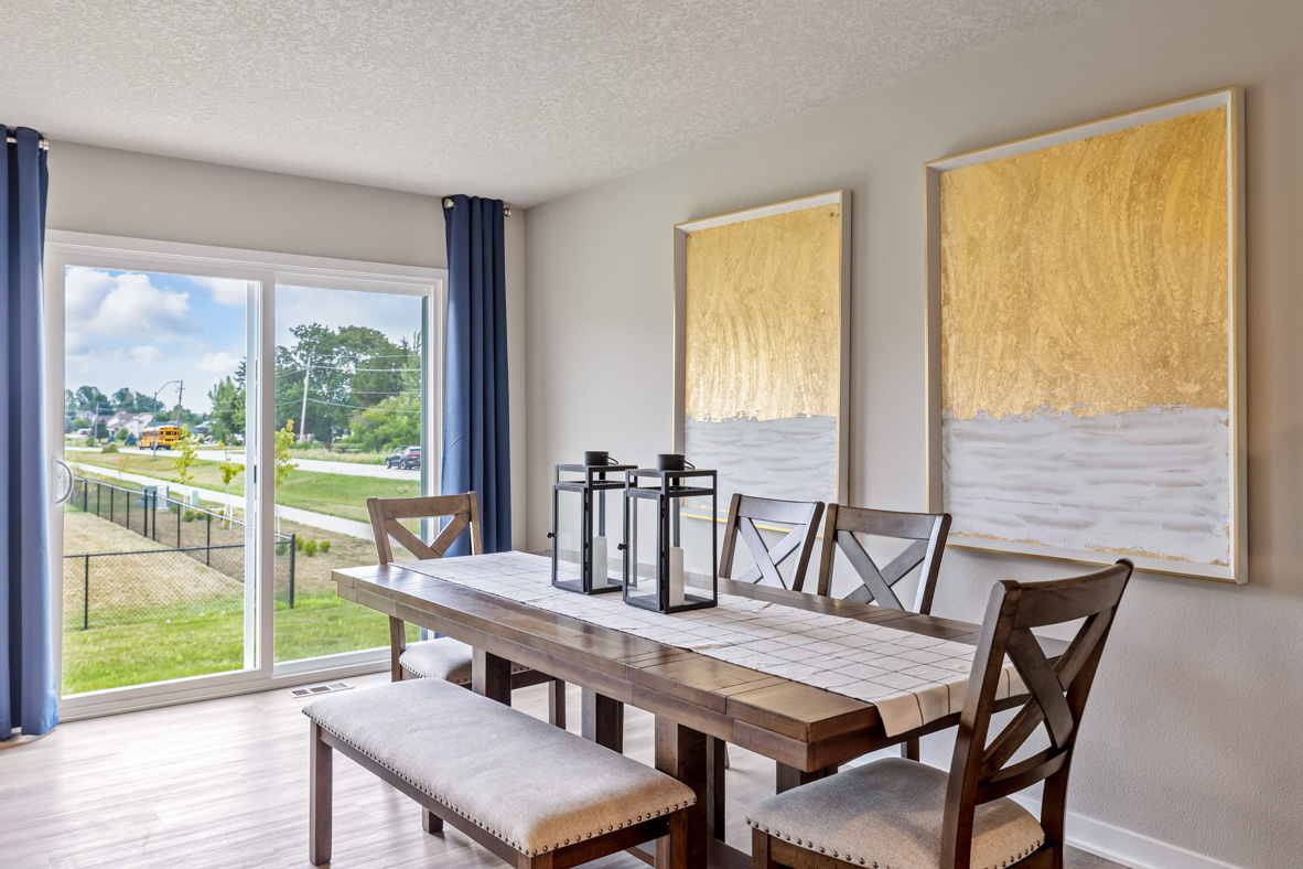 Wooden dining table, surrounded by four chairs and a bench seat, in front of sliding glass doors that provide access to the Roland's back yard.