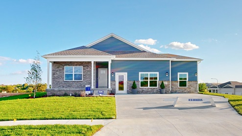 Pioneer Village's sales center, a one-story home with blue horizontal plank siding and stacked stone accents.