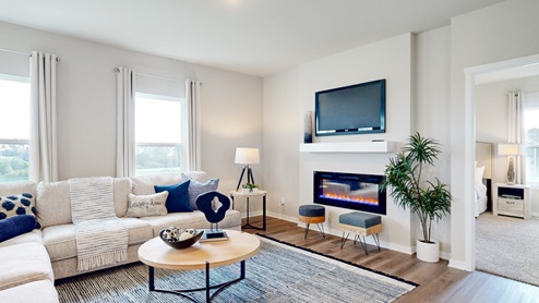 A living room with a sectional sofa, coffee and end table arranged to face the built-in electric fireplace, mantel, and wall-mounted TV on the focal wall.
