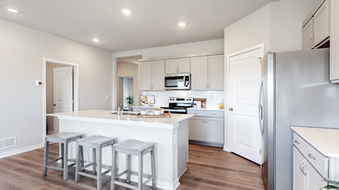 Kitchen with gray, shaker-style cabinetry, white quartz countertops, stainless-steel appliances, and an island with countertop seating.